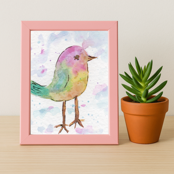 Framed 5x7 whimsical bird art print with pink frame and potted plant on a light wood surface